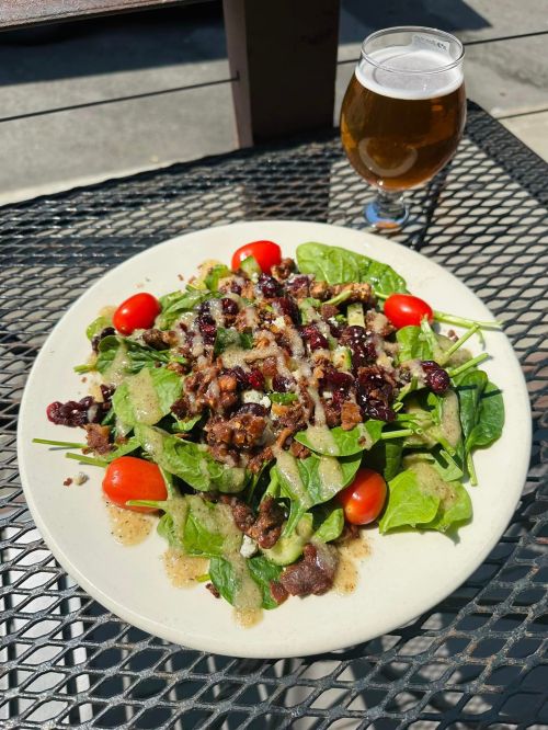 A fresh spinach salad topped with cherry tomatoes, nuts, and dressing, alongside a glass of beer on a table.