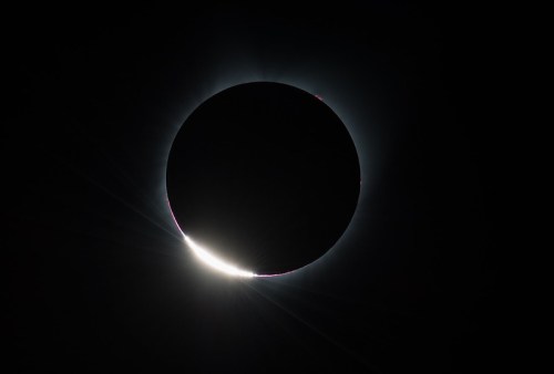A solar eclipse with a darkened sun surrounded by a glowing corona and rays of light extending outward.
