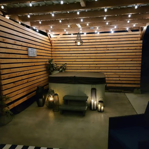 Cozy outdoor space with wooden walls, string lights, a hot tub, and decorative lanterns.