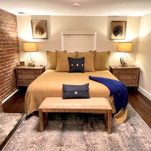 Cozy bedroom with a yellow bedspread, two nightstands, lamps, and a bench at the foot of the bed. Warm, inviting decor.