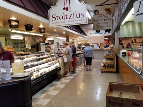 A bustling bakery with customers browsing pastries and fresh salads in a market setting.