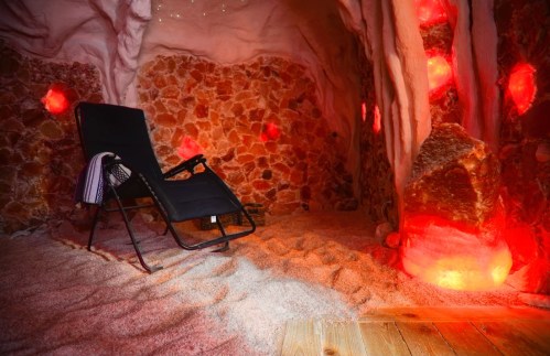 A cozy salt room with a reclining chair, illuminated by red lights and surrounded by salt rock walls.