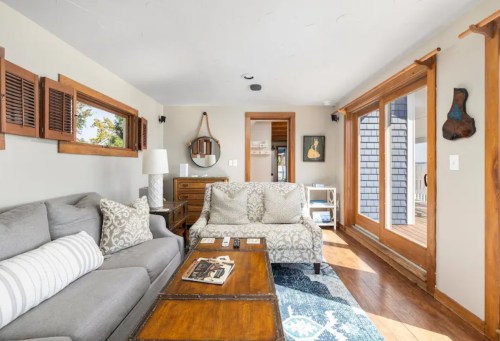 Cozy living room with gray sofas, wooden accents, and large windows letting in natural light.