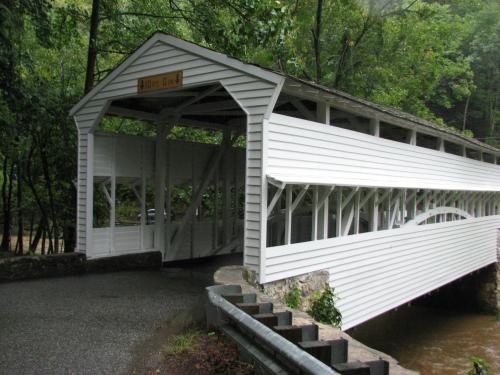 A white covered bridge with a sign reading "Hoot Owl," surrounded by lush green trees and a river below.