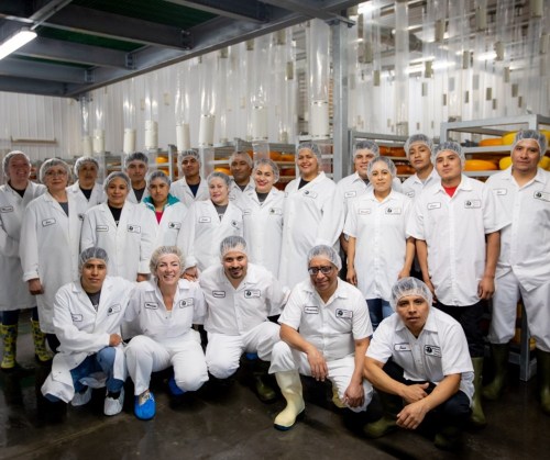 A group of workers in white lab coats and hairnets pose together in a food production facility.