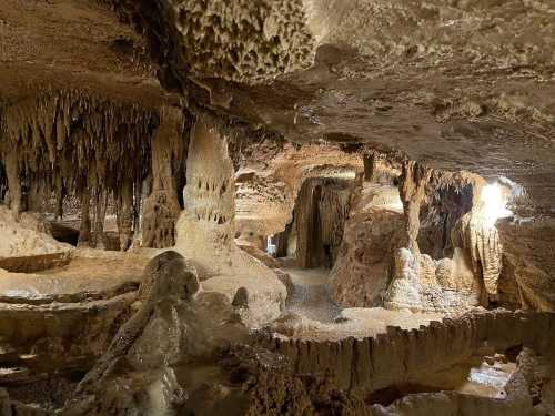 A dimly lit cave interior featuring stalactites and stalagmites, with rocky formations and a winding pathway.