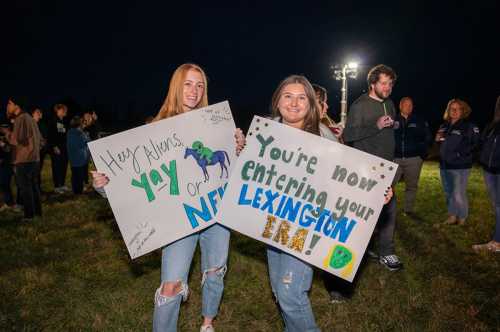 Two young women hold colorful signs at a nighttime event, celebrating a new era with excitement and enthusiasm.