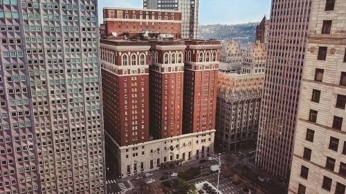 Aerial view of a historic red brick building surrounded by modern skyscrapers in an urban setting.
