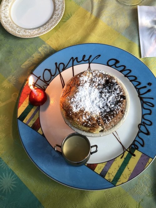A plate with a pancake topped with powdered sugar, a strawberry, and a small container of syrup, with a candle beside it.