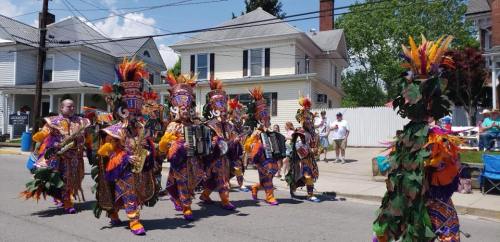 Colorful performers in elaborate costumes march in a parade, playing accordions and celebrating in a festive atmosphere.
