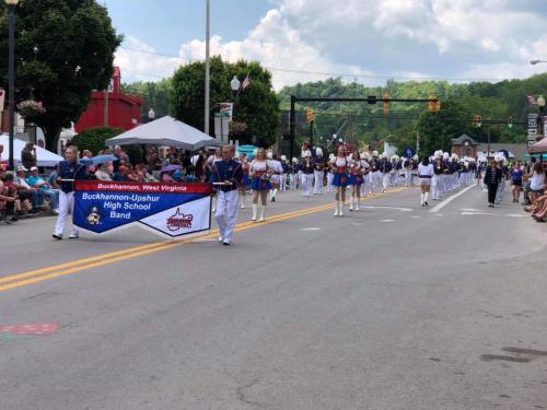 A parade featuring the Buckhannon-Upshur High School Band marching down a street with spectators on both sides.
