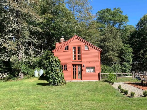 A red house surrounded by greenery, with large windows and a well-maintained lawn under a clear blue sky.