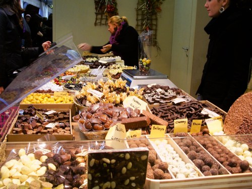 A colorful display of various chocolates and sweets at a market stall, with customers browsing the treats.
