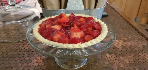 A glass pie dish holds a strawberry pie topped with bright red strawberries and a glossy glaze.