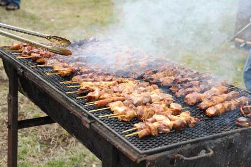 Grilled skewers of meat sizzling on a barbecue grill, surrounded by smoke in an outdoor setting.