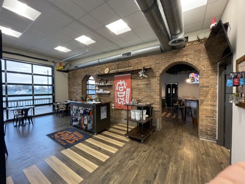 A cozy café interior with brick walls, wooden flooring, and a counter displaying snacks and drinks, overlooking a window.