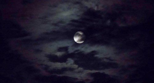 A full moon partially obscured by dark, swirling clouds in a night sky.