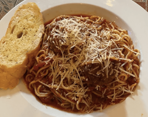 A plate of spaghetti with meatballs, topped with cheese, served with a slice of garlic bread on the side.
