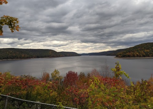 A serene lake surrounded by autumn foliage under a cloudy sky, with hills in the background.