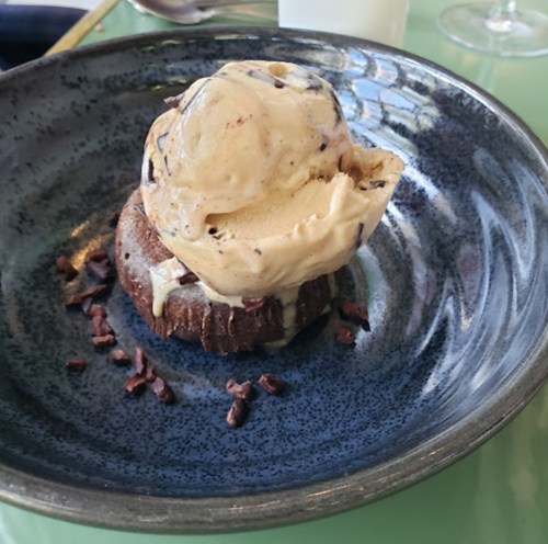 A chocolate dessert topped with a scoop of ice cream, served on a dark blue plate with chocolate shavings.