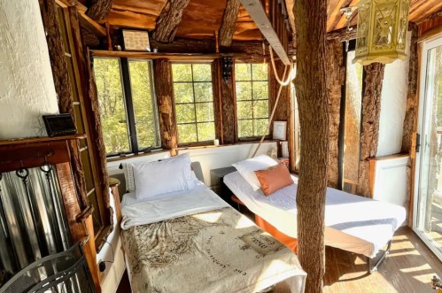 Cozy interior of a rustic cabin with two beds, wooden beams, and large windows letting in natural light.
