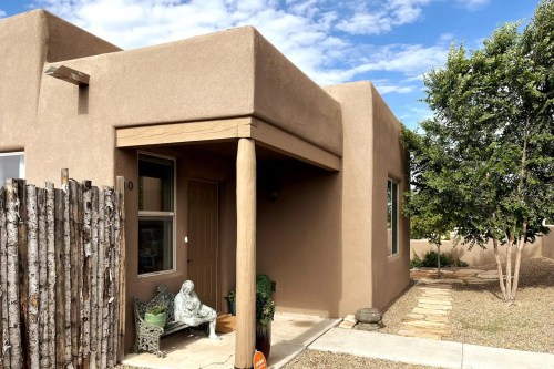 A southwestern-style home with a stucco exterior, wooden posts, and a small garden area. A statue sits by the entrance.