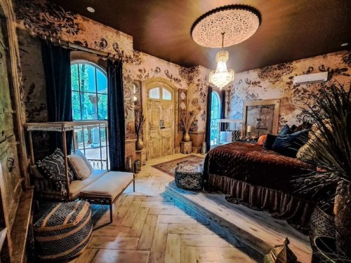 Cozy bedroom with ornate decor, a chandelier, and large windows, featuring rich textures and warm colors.