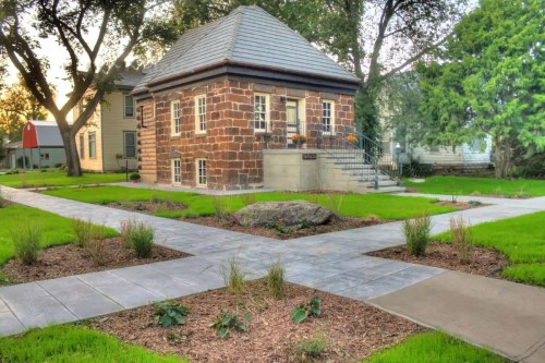 A small stone building with a sloped roof surrounded by landscaped paths and greenery in a residential area.