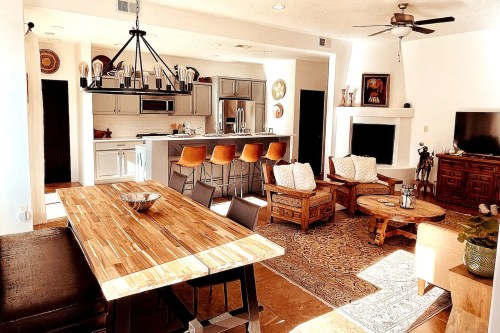 A modern living space featuring a dining table, kitchen bar, cozy seating area, and a warm color palette.