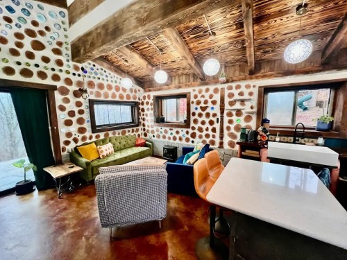 Cozy interior of a rustic home with colorful walls, a green sofa, and a modern kitchen area. Natural light filters in.