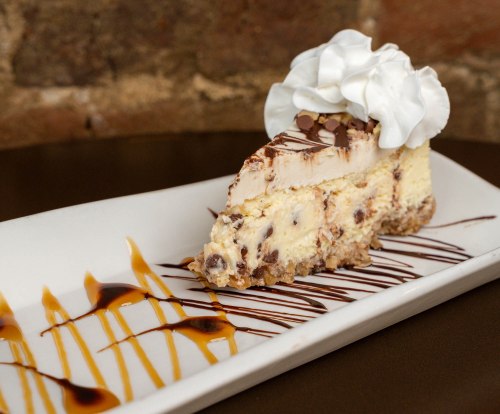 A slice of dessert topped with whipped cream, drizzled with chocolate and caramel sauce on a white plate.