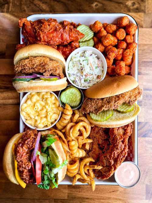 A tray filled with fried chicken sandwiches, crispy chicken wings, coleslaw, macaroni and cheese, and curly fries.