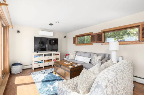 Cozy living room with a gray sofa, wooden coffee table, TV, and large windows letting in natural light.