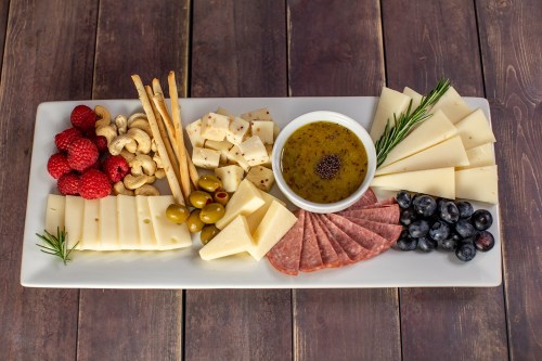 A cheese platter featuring various cheeses, nuts, olives, berries, and a bowl of dipping oil on a wooden table.