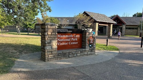Sign for Mammoth Cave National Park Visitor Center, with a stone structure and trees in the background.