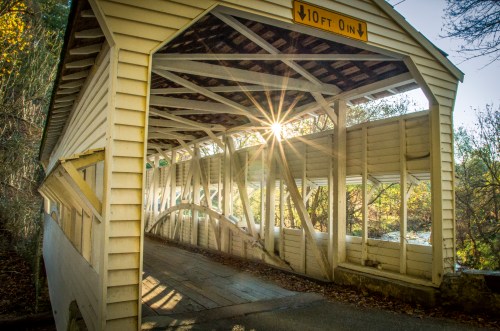 A sunbeam shines through the interior of a covered bridge, highlighting its wooden structure and surrounding nature.