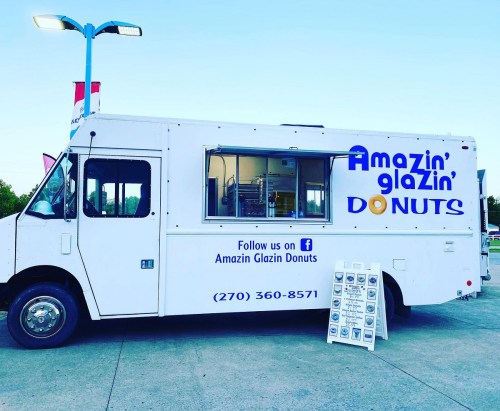 A white food truck with "Amazin' Glazin' Donuts" signage parked, featuring a menu board in front.