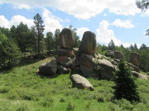 A cluster of large boulders surrounded by green grass and trees under a partly cloudy sky.