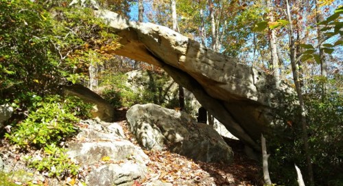 A large rock formation arches over a path, surrounded by trees and autumn foliage.