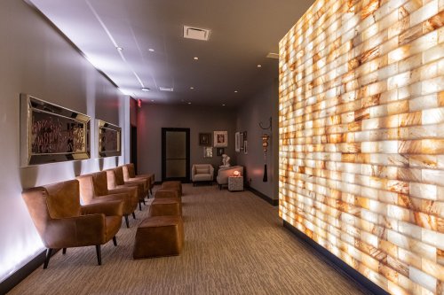 A modern waiting area with brown chairs, soft lighting, and a textured wall made of illuminated stone.