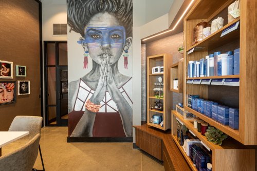 A stylish interior featuring a mural of a woman and shelves with skincare products.