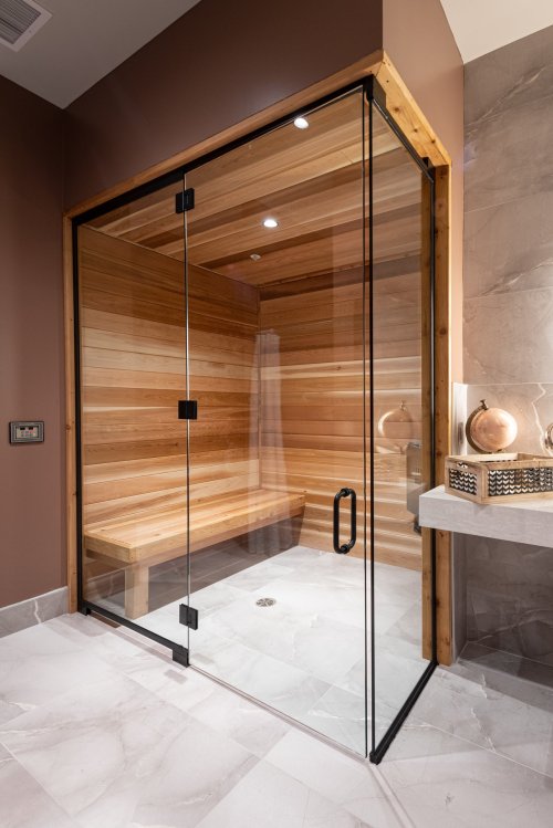 A modern sauna with wooden walls, glass doors, and a sleek marble floor in a stylish bathroom setting.