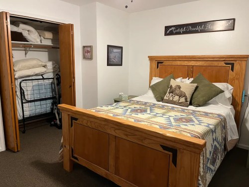 Cozy bedroom with a wooden bed, decorative quilt, and a closet with extra bedding visible.