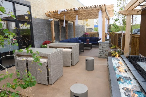 A cozy outdoor patio with a pergola, seating area, and a water feature, surrounded by greenery and flowers.