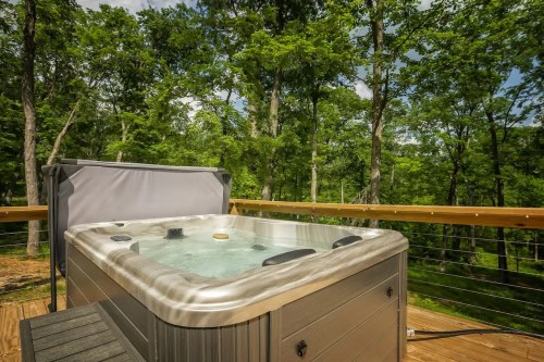 A hot tub on a wooden deck surrounded by lush green trees and a clear blue sky.