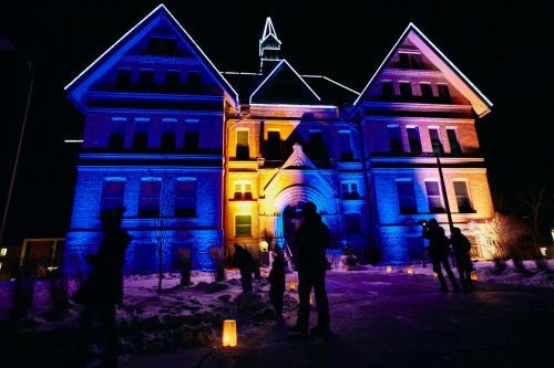 A historic building illuminated with blue and orange lights at night, with silhouettes of people in the foreground.