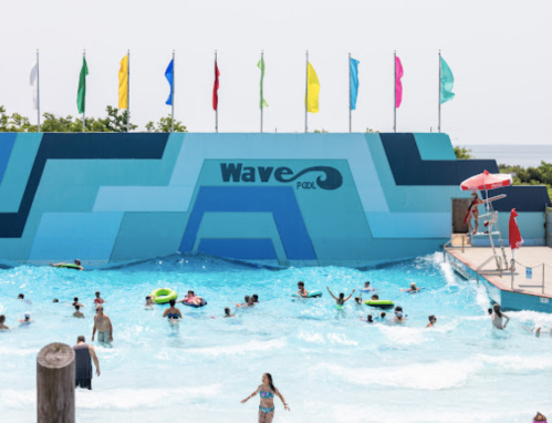A vibrant wave pool with colorful flags, people enjoying the water, and a lifeguard station nearby.