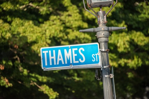 Street sign for Thames Street, mounted on a lamp post with green trees in the background.