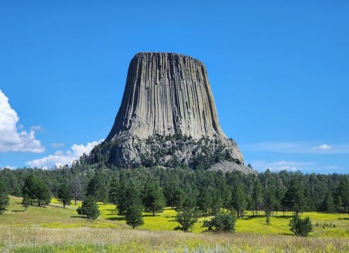 A tall, flat-topped rock formation rises above a green landscape under a clear blue sky.