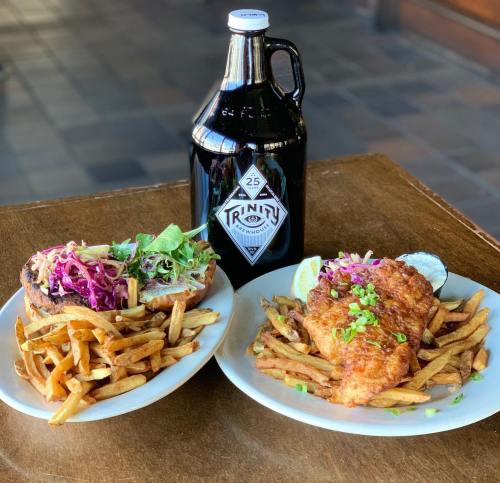 A plate of crispy fish and fries with a side salad, alongside a growler of beer on a wooden table.